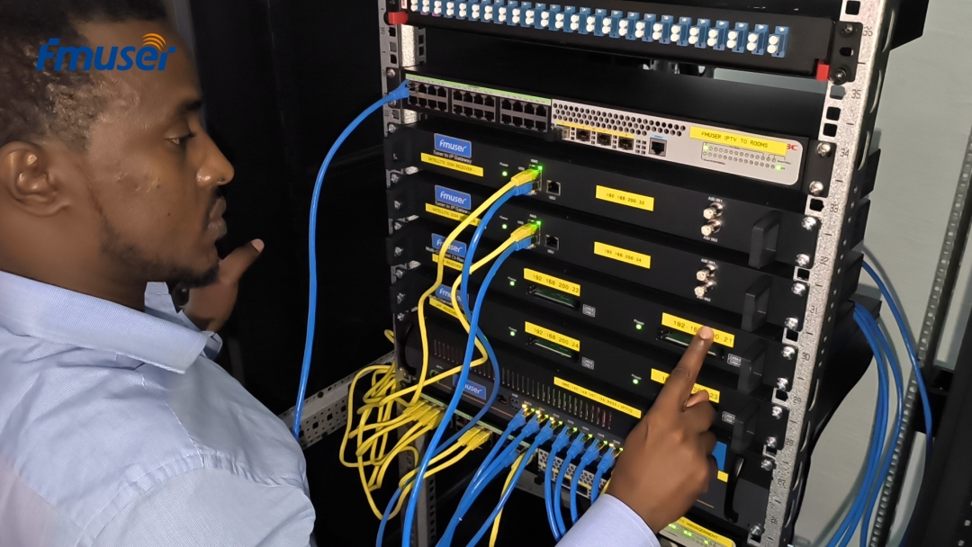 An engineer performs on-site configuration and testing on the FMUSER smart hotel TV system headend rack. The robust setup features multiple FMUSER receivers and gateways, clearly labeled for easy network management, demonstrating the system's reliable hardware integration and strong support for global hotel projects.